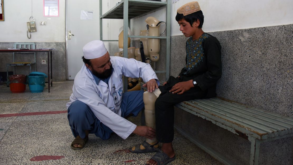 Dem Jungen wird von einem HI-Therapeuten, der vor ihm kniet, seine Prothese angepasst. 