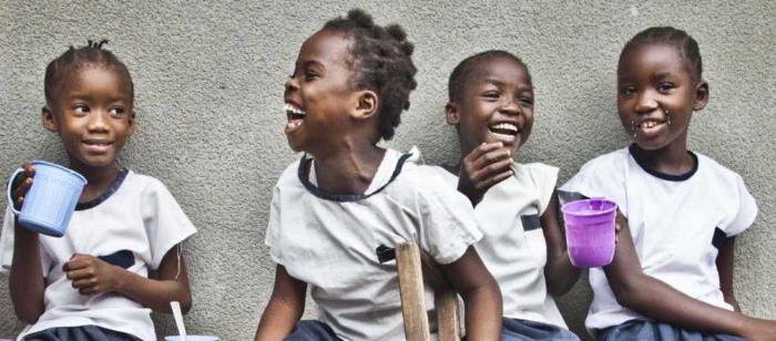 Lachende Schulkinder aus der Demokratischen Republik Kongo, ein Mädchen stützt sich auf eine Gehhilfe