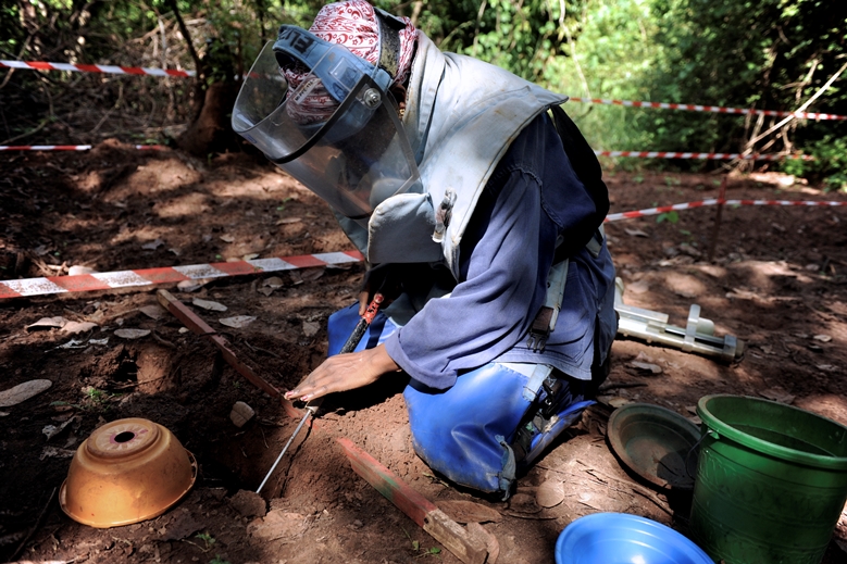 senegal-elizabeth-entminung Das Bild zeigt Elizabeth bei einer Entminung. Sie trägt schwere Schutzkleidung und ein Visier. Kniend befindet sie sich in einer abgesperrten Zone und tastet eine Mine ab